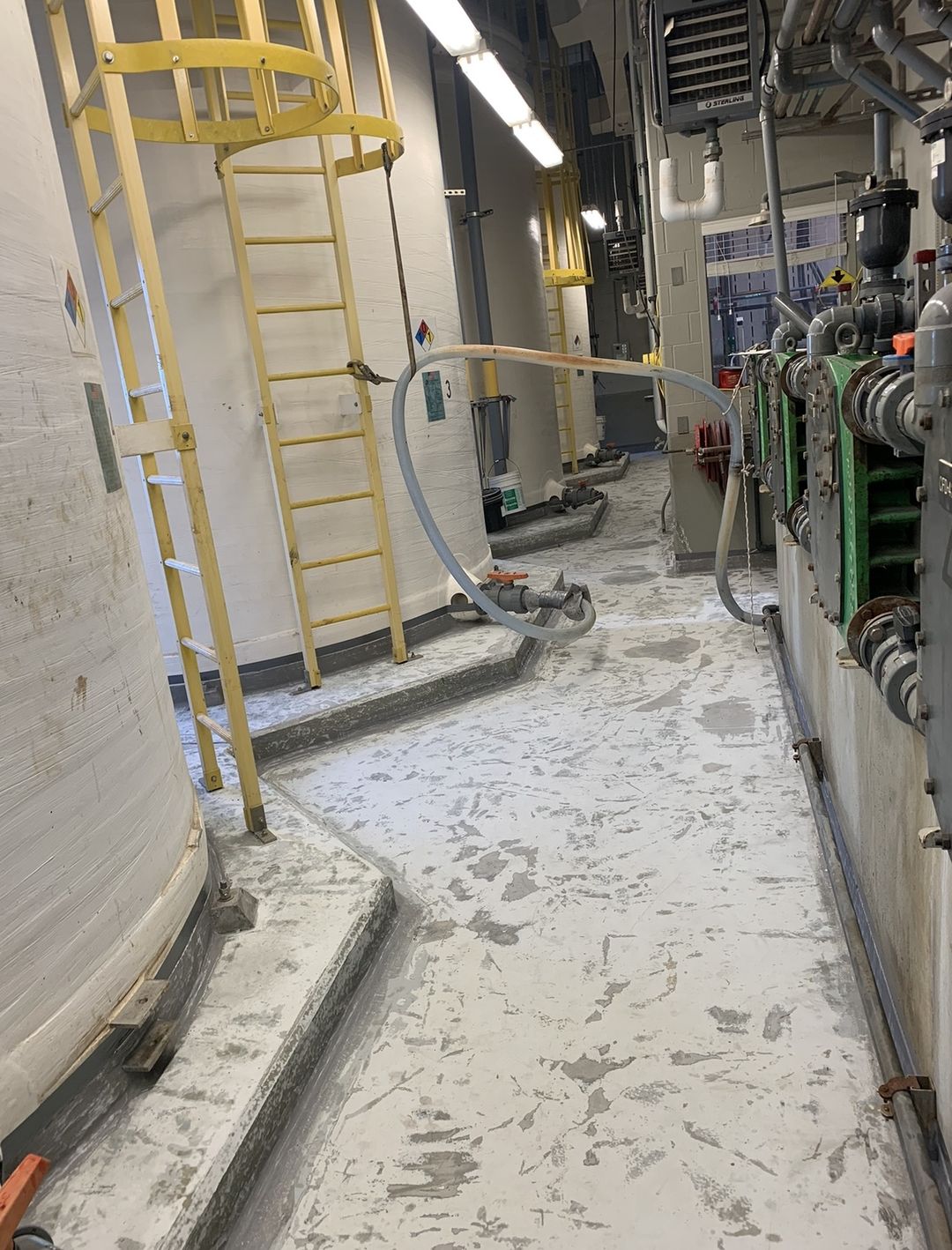 Chemical storage containment area before recoating, with stained and spalled concrete around storage tanks