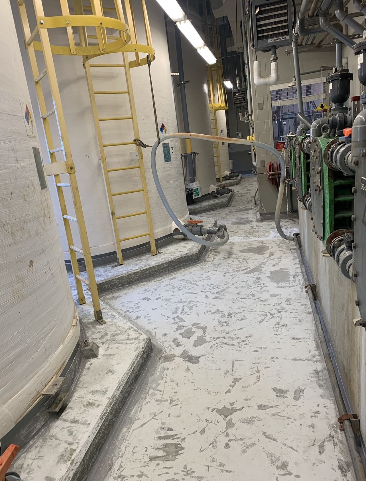 Chemical storage containment area before recoating, with stained and spalled concrete around storage tanks