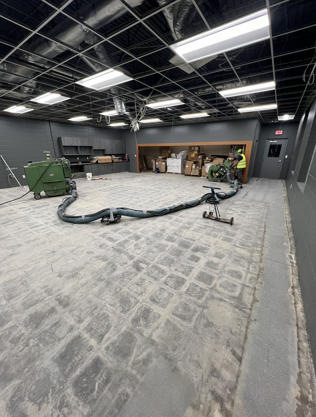 Commercial room during surface preparation, with tile adhesive being ground off the concrete and dust-collection equipment in use