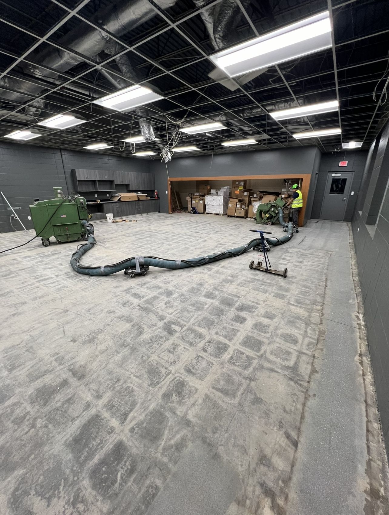 Commercial room during surface preparation, with tile adhesive being ground off the concrete and dust-collection equipment in use