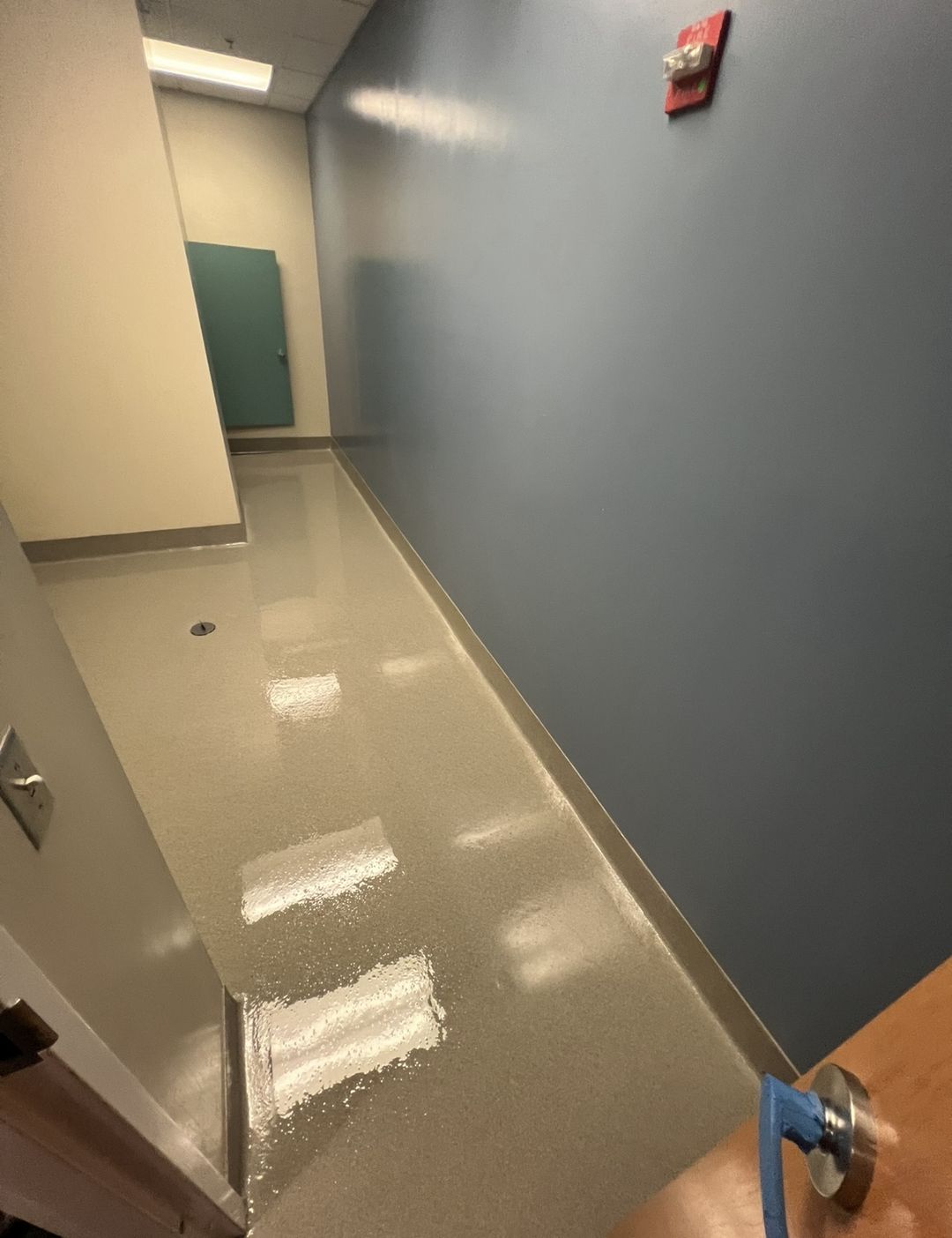 The same corridor finished with a seamless light flake floor, integral cove base and a recessed floor drain