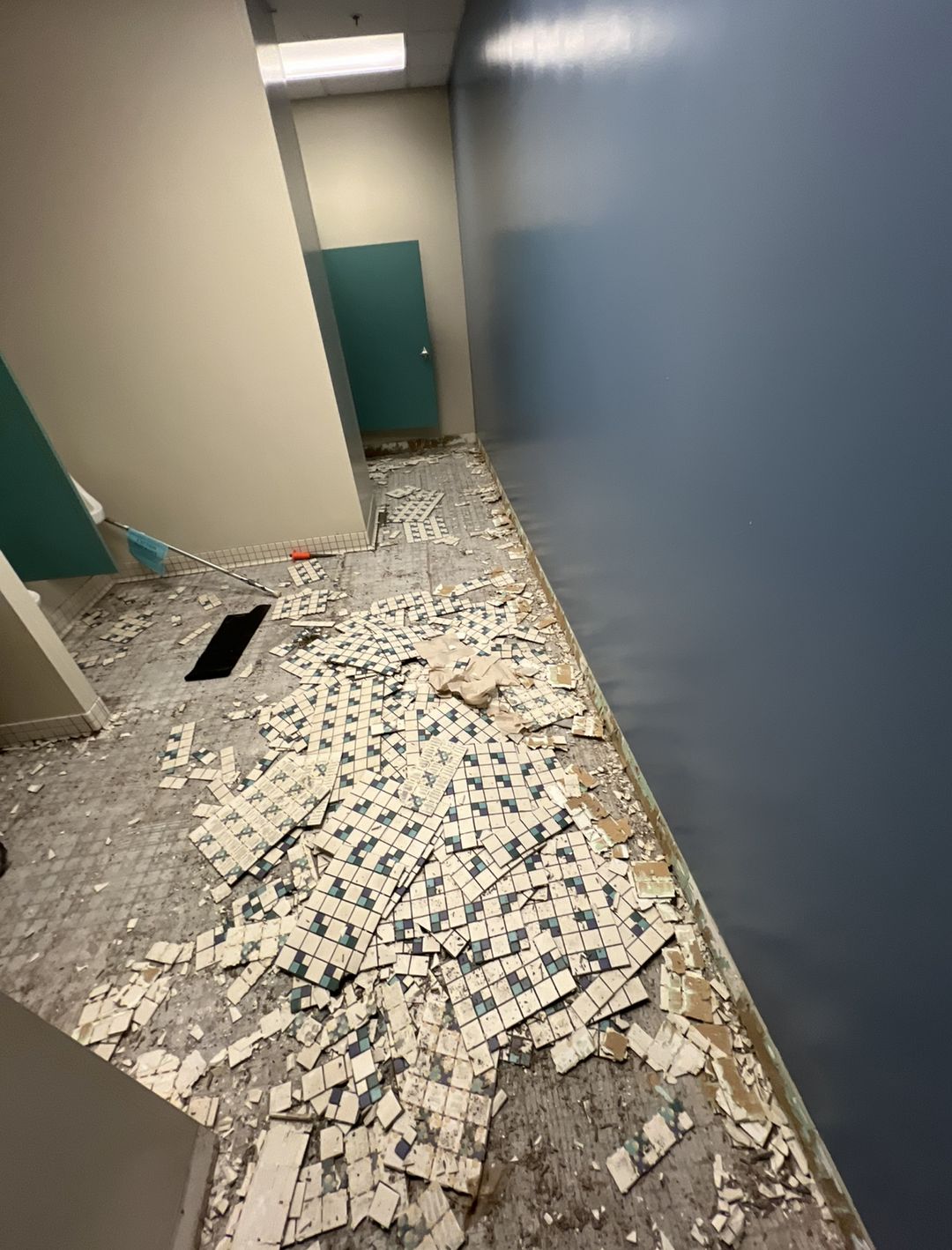 Commercial corridor mid-demolition with old mosaic tile broken up across the floor