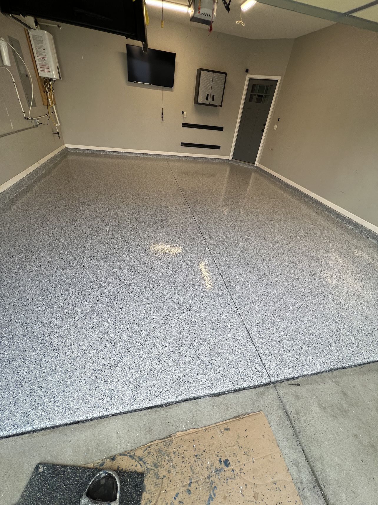 The same garage after coating, with a grey, white and black flake epoxy floor and a clean edge along the wall base