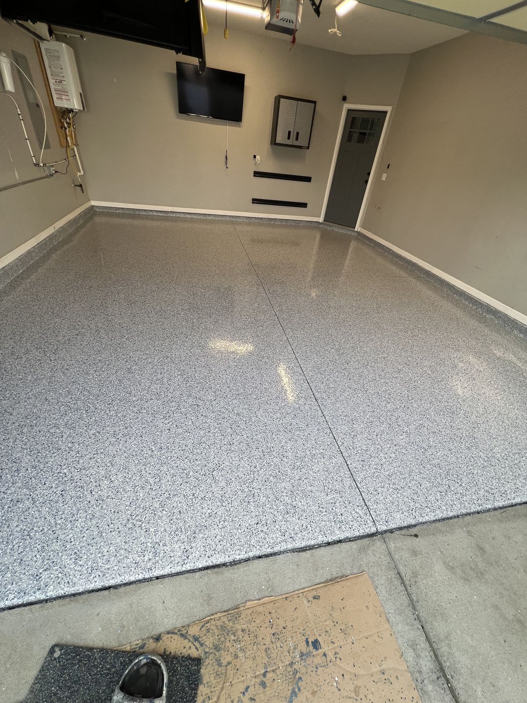 The same garage after coating, with a grey, white and black flake epoxy floor and a clean edge along the wall base