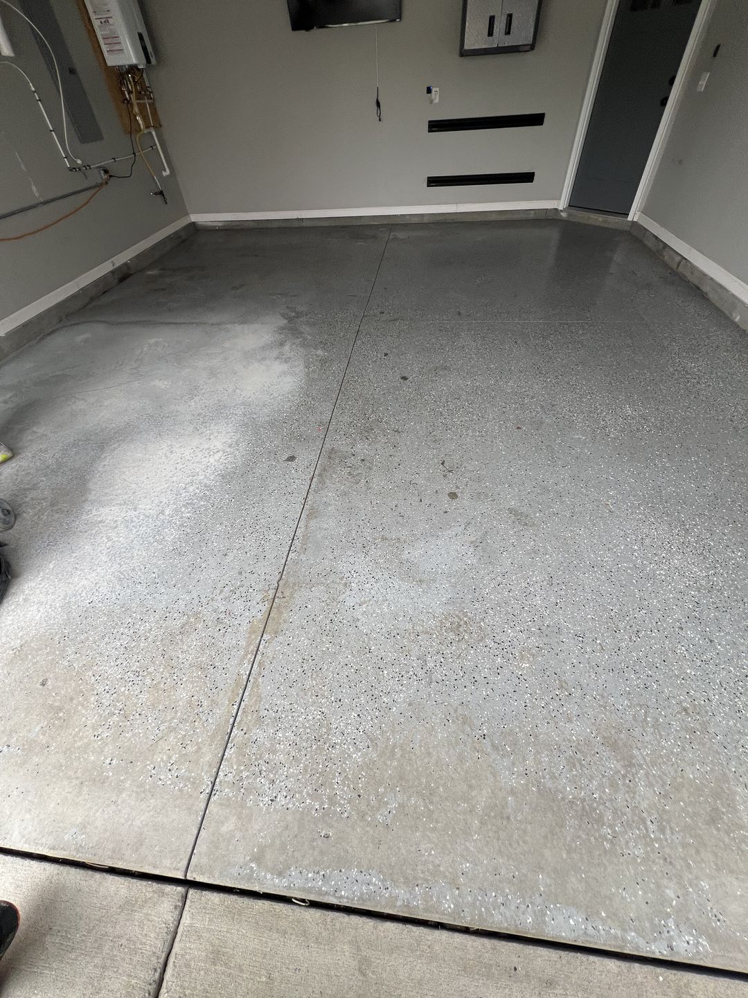 Bare grey concrete garage slab before coating, with a water heater and electrical panel on the wall