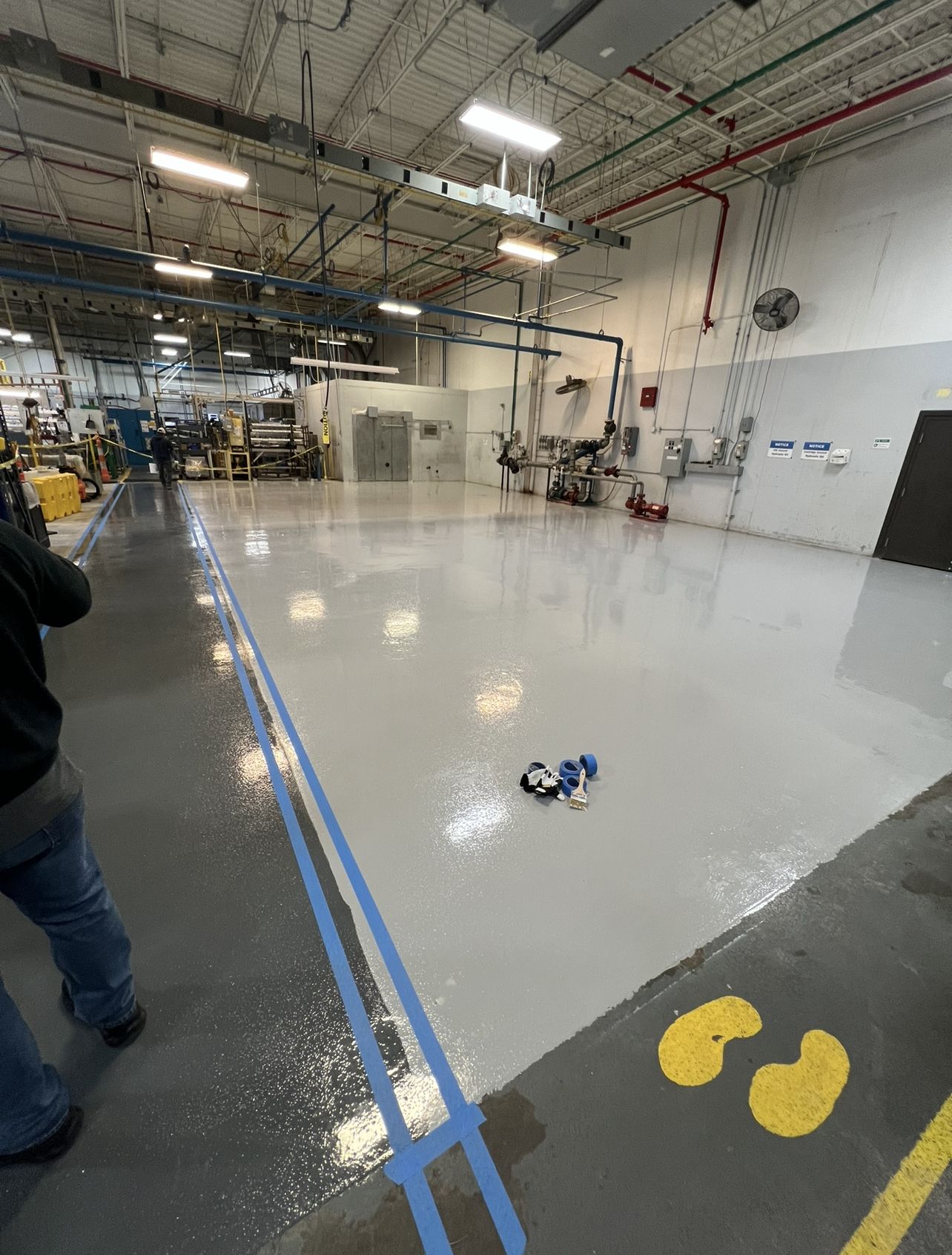 The same manufacturing bay after coating, with a high-gloss grey epoxy floor, blue safety lines and yellow walkway markings