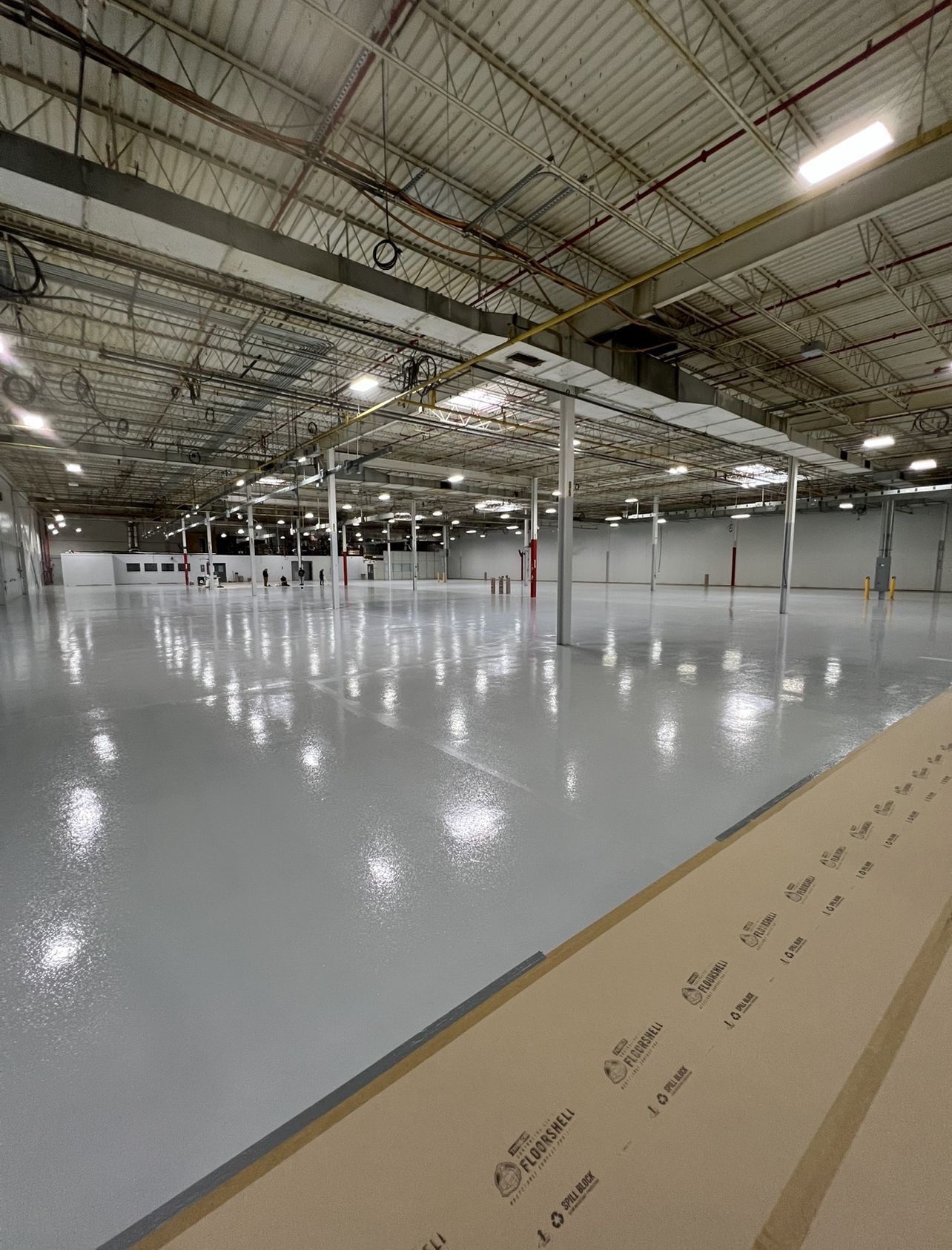 Newly coated high-gloss grey epoxy floor stretching across a large industrial plant bay