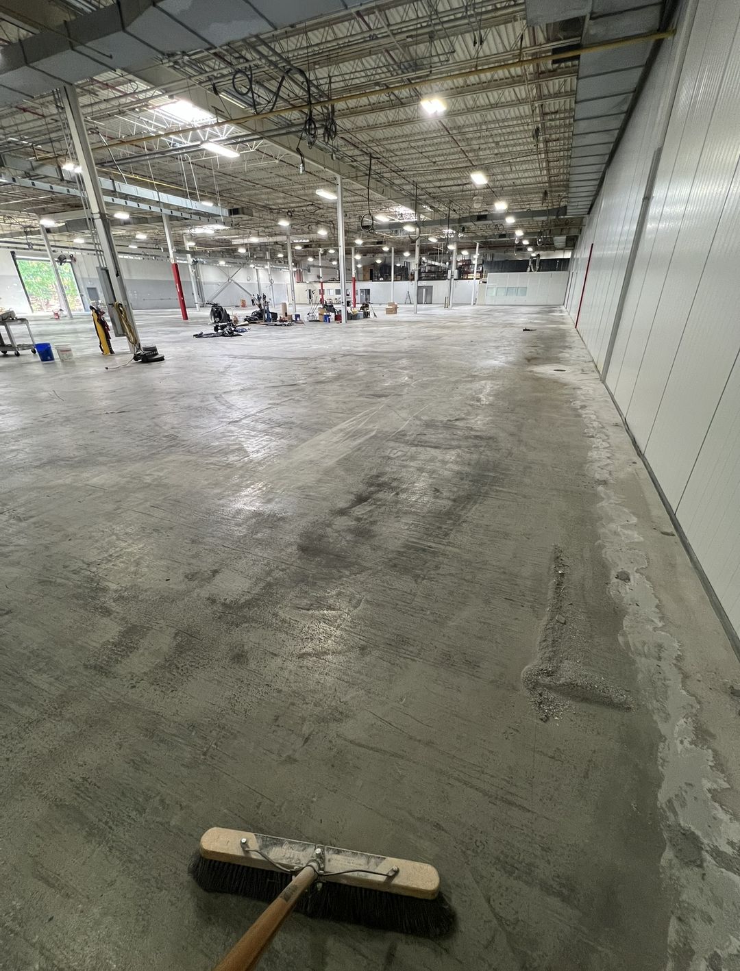 Large empty warehouse bay with bare, patched and stained concrete before coating