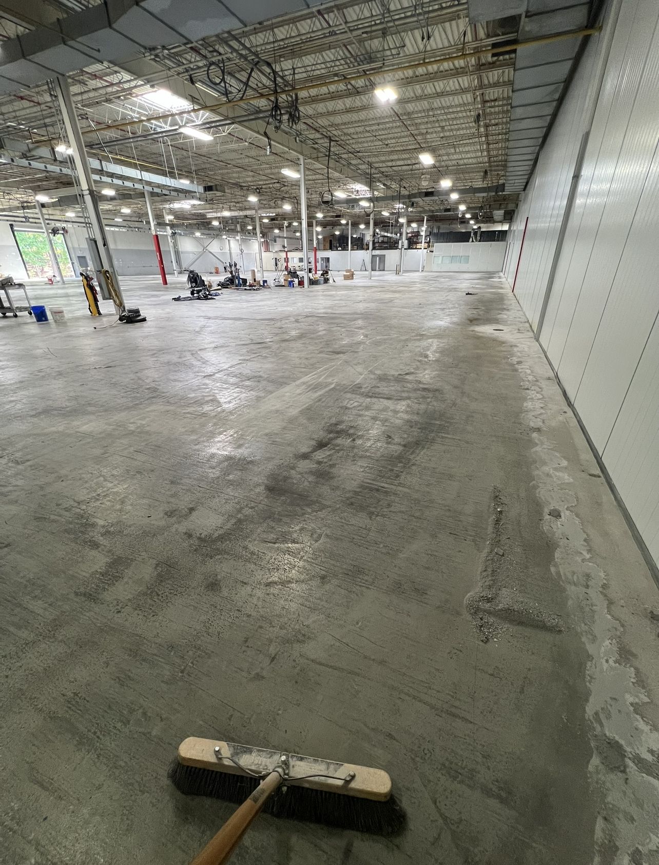 Large empty warehouse bay with bare, patched and stained concrete before coating